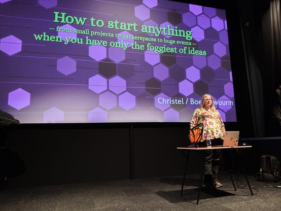 Photo of boekenwuurm starting their presentation, title as mentioned in post, green letters on a purple background.