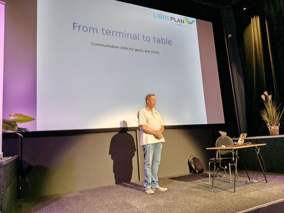 Jeroen Baten on stage of his opening slide titled "From terminal to table -- Communication skills for geeks and nerds"