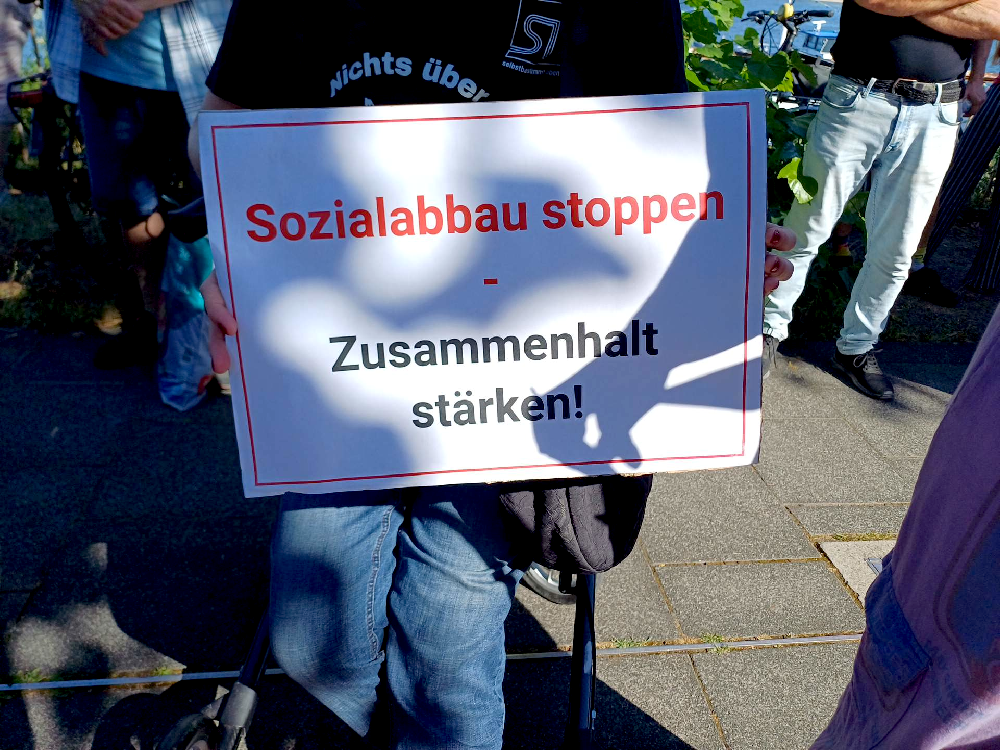 Eine Demonstrantin hält ein Schild: "Sozialbbau stoppen - Zusammenhalt stärken!"
